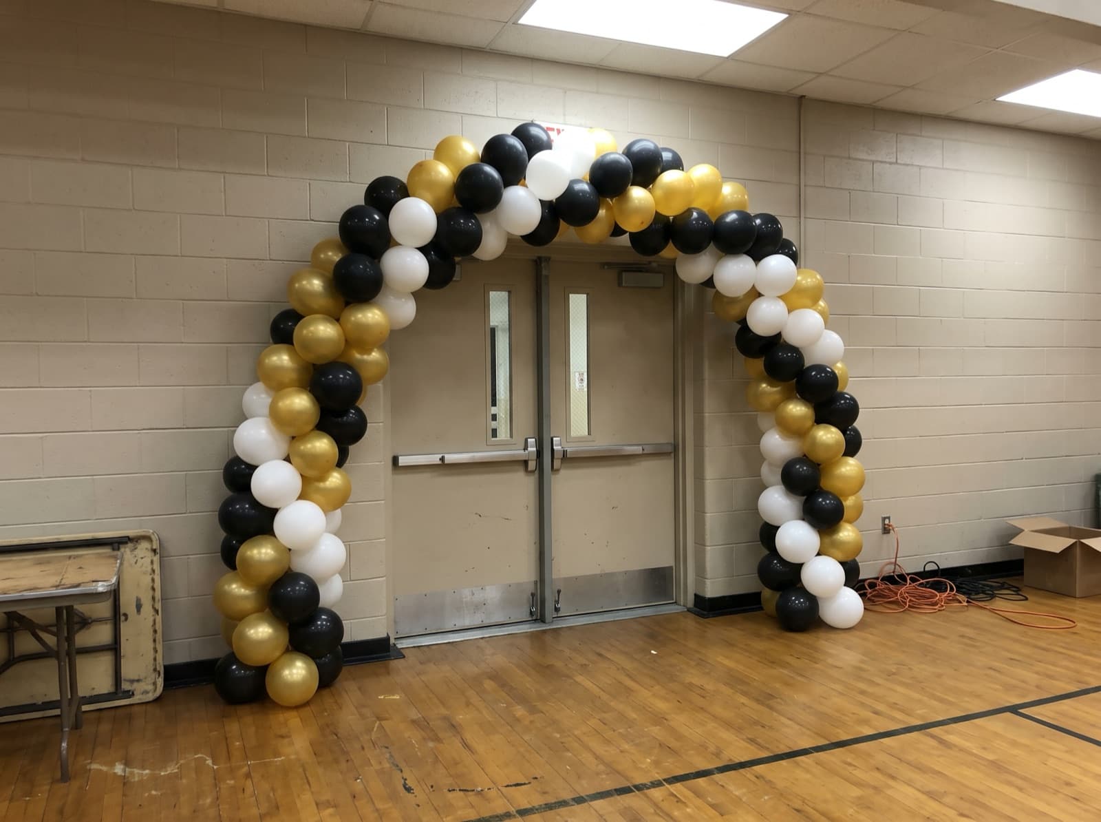 Spiral balloon arch in black and gold over a gym entrance